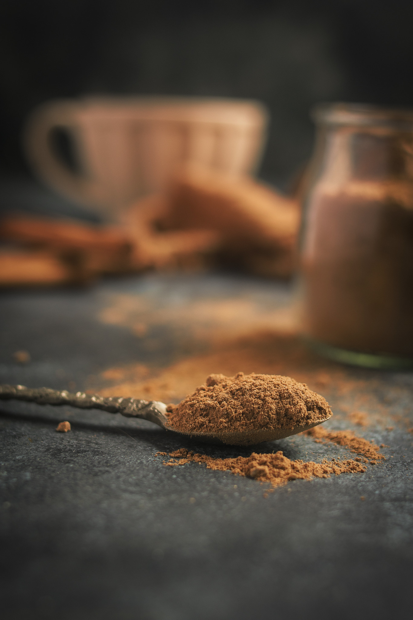 Spoonful of homemade pumpkin pie spice with a glass jar and cup softly blurred in the background.